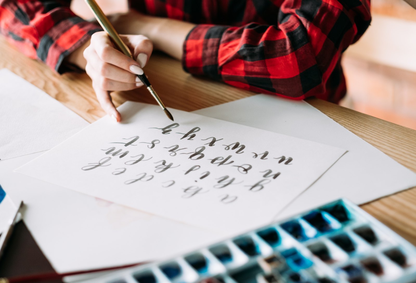 Hand lettering a brush script alphabet with a watercolor palette nearby