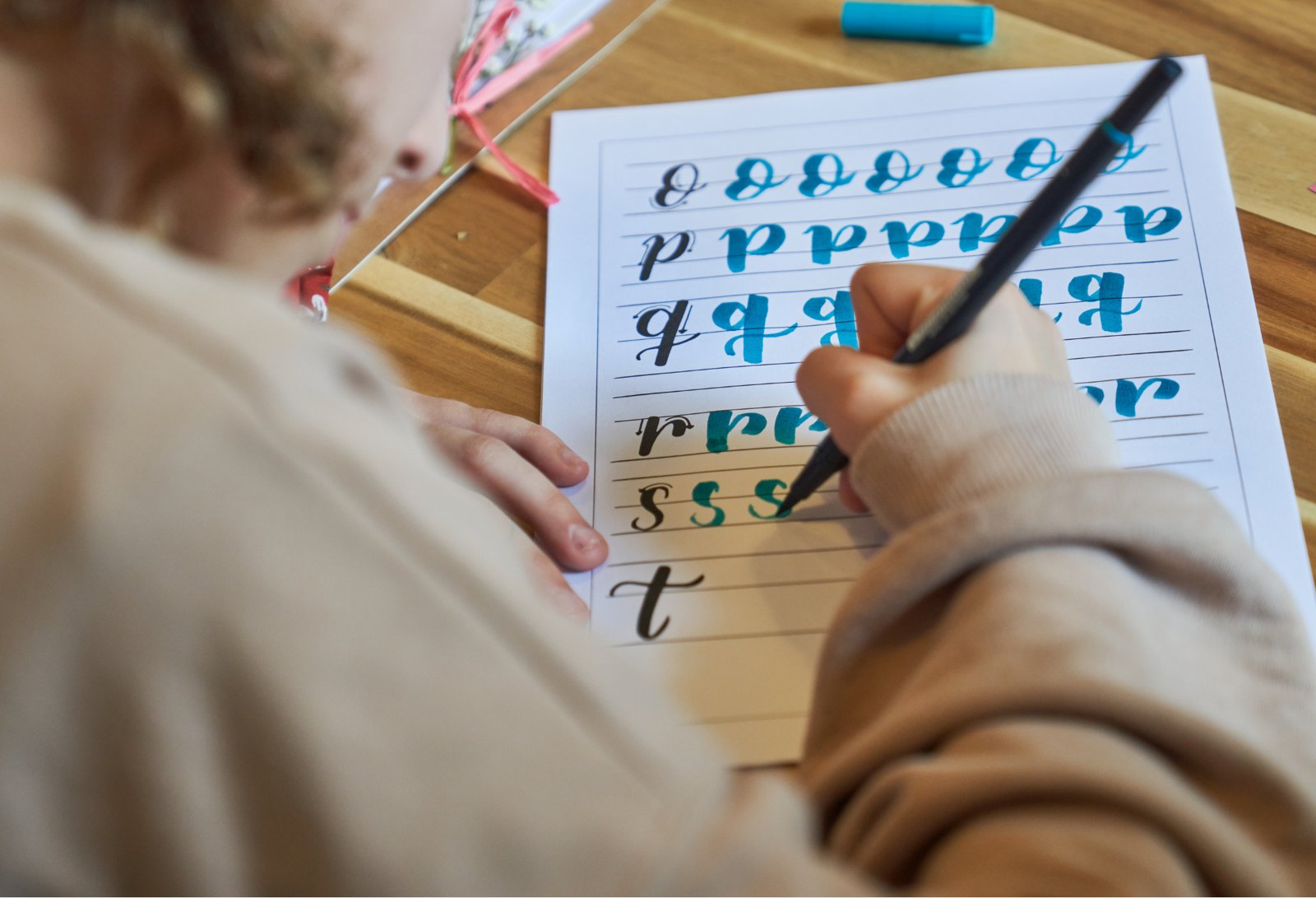 Beginner tracing teal brush letters on a lettering practice worksheet